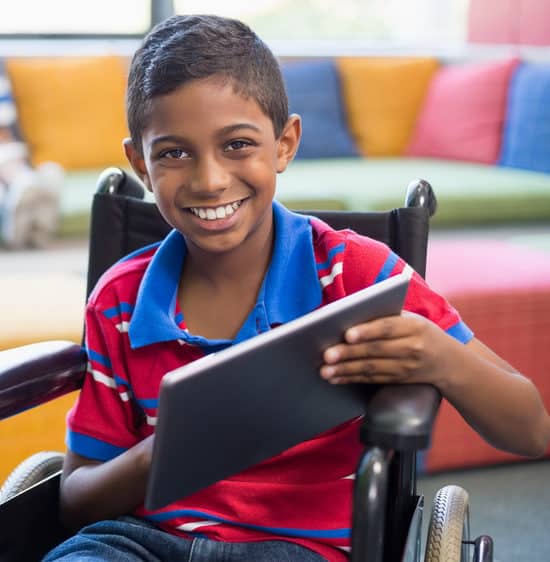 Disabled schoolboy on wheelchair using digital tablet in library