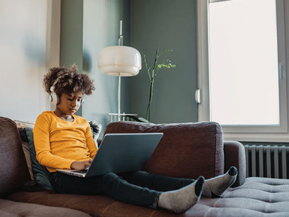 Young woman sitting on couch working on laptop
