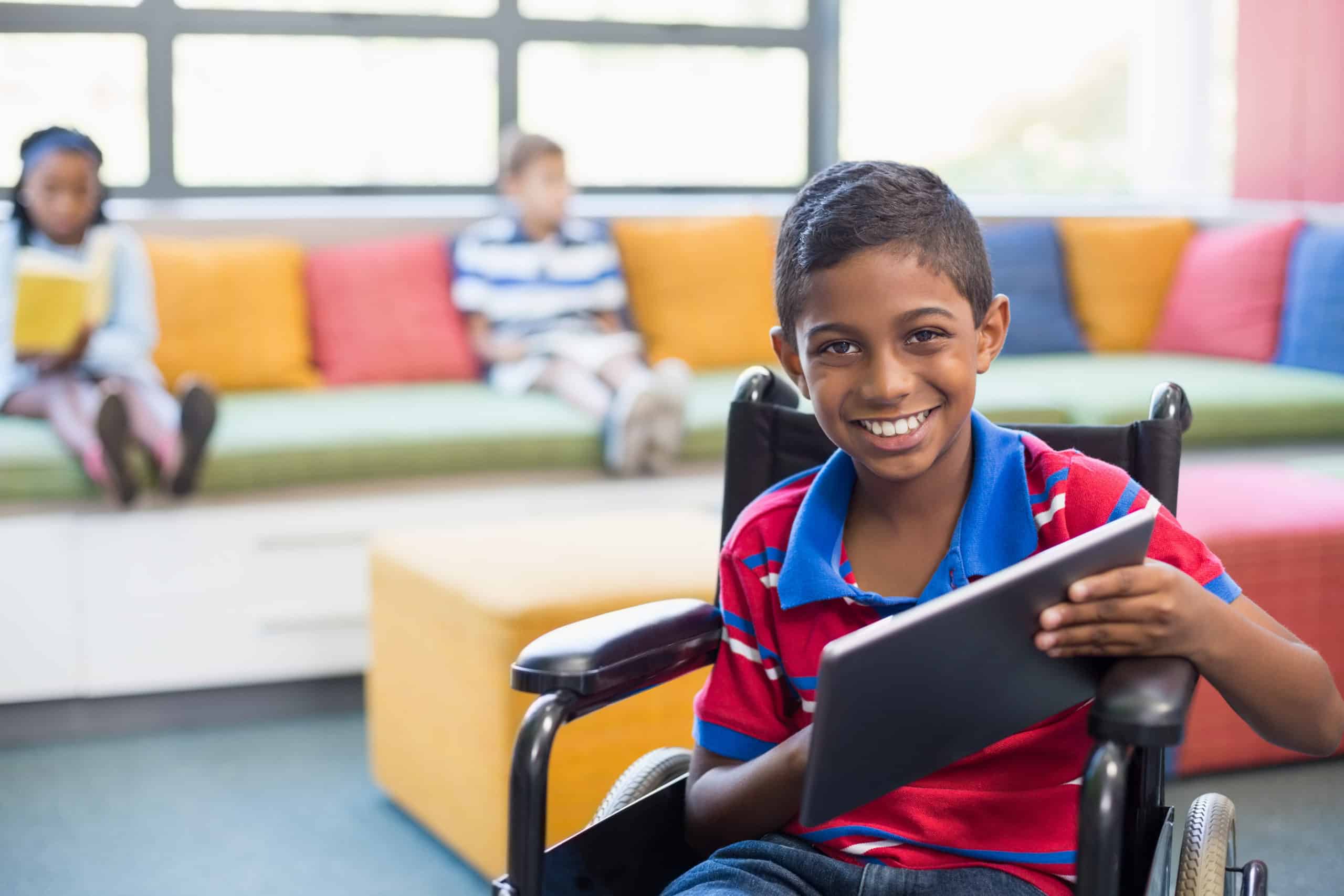 Portrait of disabled schoolboy on wheelchair using digital tablet in library at school