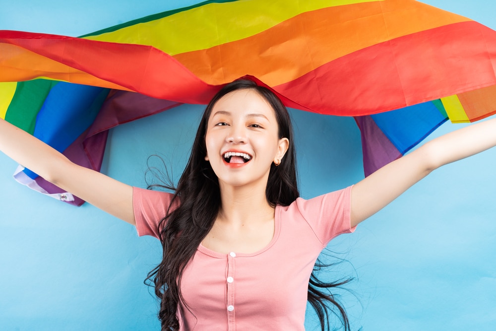 Young Asian woman holding rainbow flag to support LGBTQ+ community