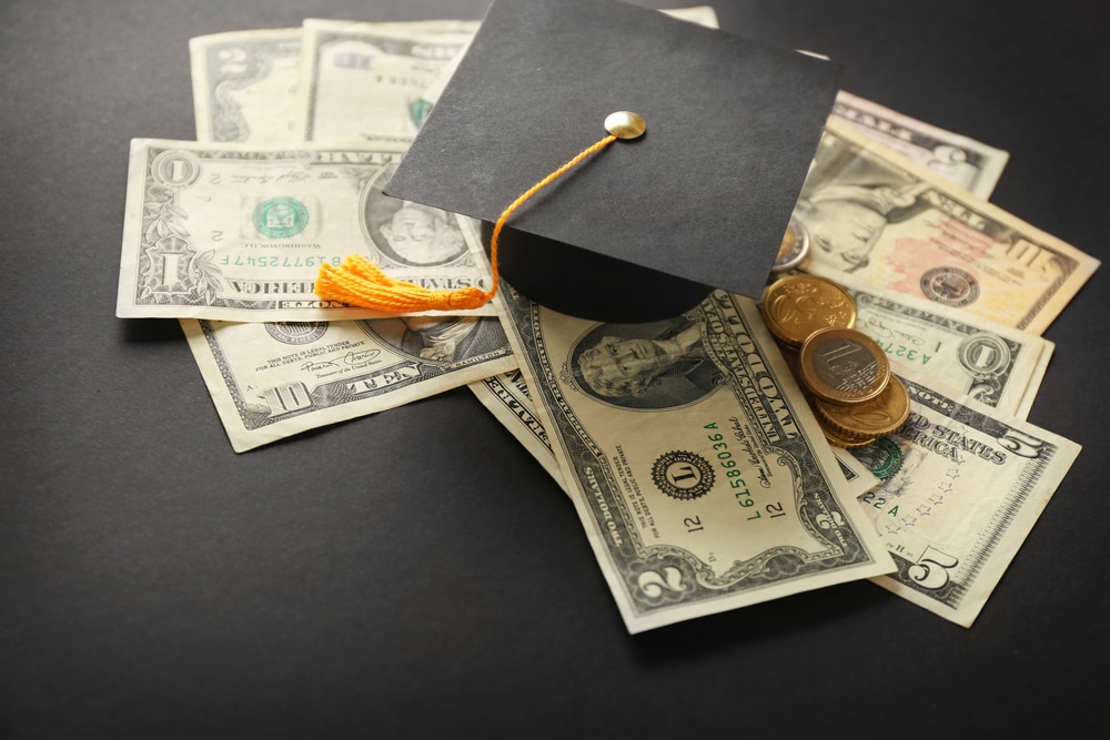 Graduation hat, dollar banknotes and coins on dark table. Pocket money concept