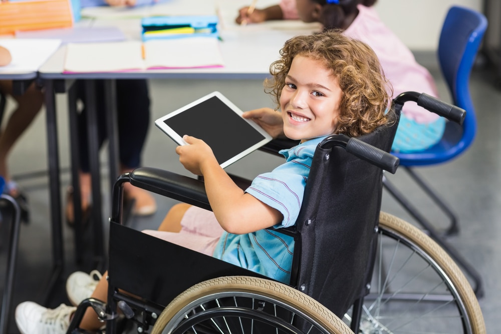 Portrait of disabled schoolboy using digital tablet in classroom at school