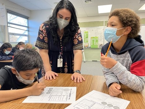 Student Teacher helping two students with masks on complete resiliency forms