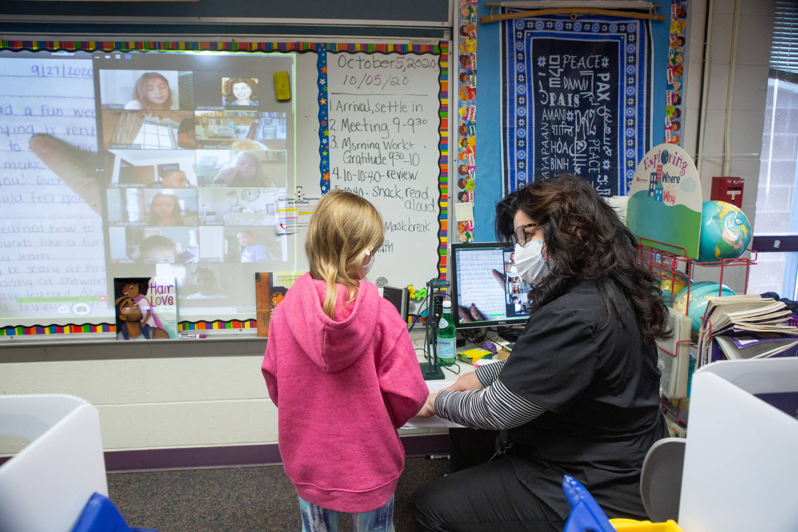 A second-grade teacher helps a student with a writing assignment in a hybrid classroom.
