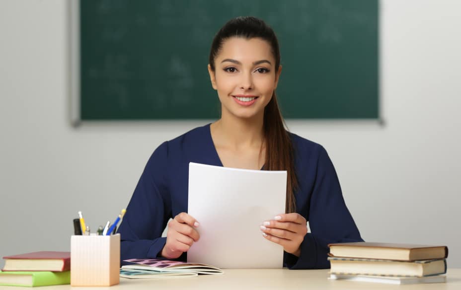 Beautiful young teacher sitting at table in classroom