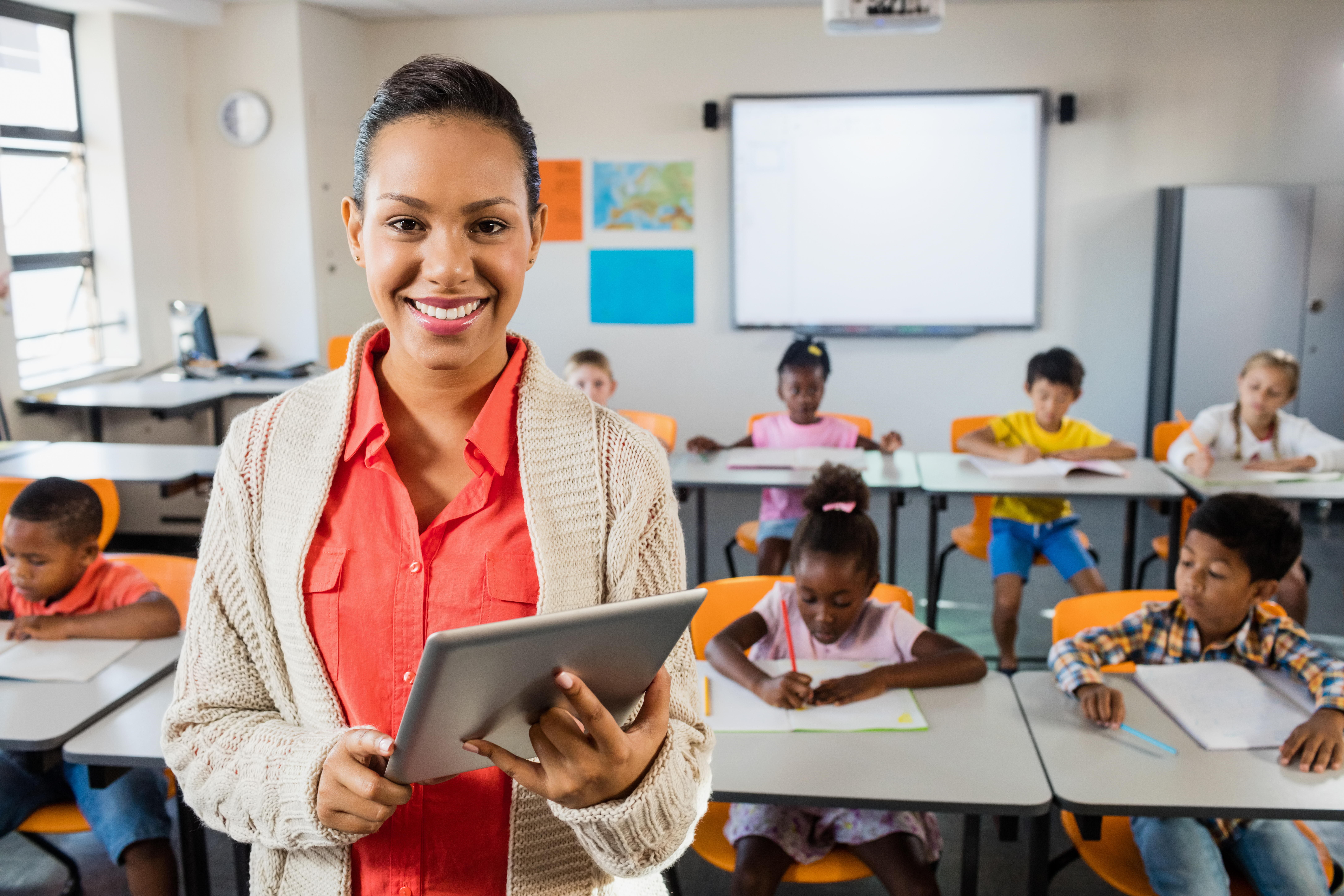 Teacher posing in front of class with tablet pc at elementary school